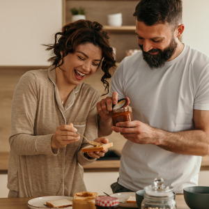 Partners sharing morning meal, spreading jam on toast together.