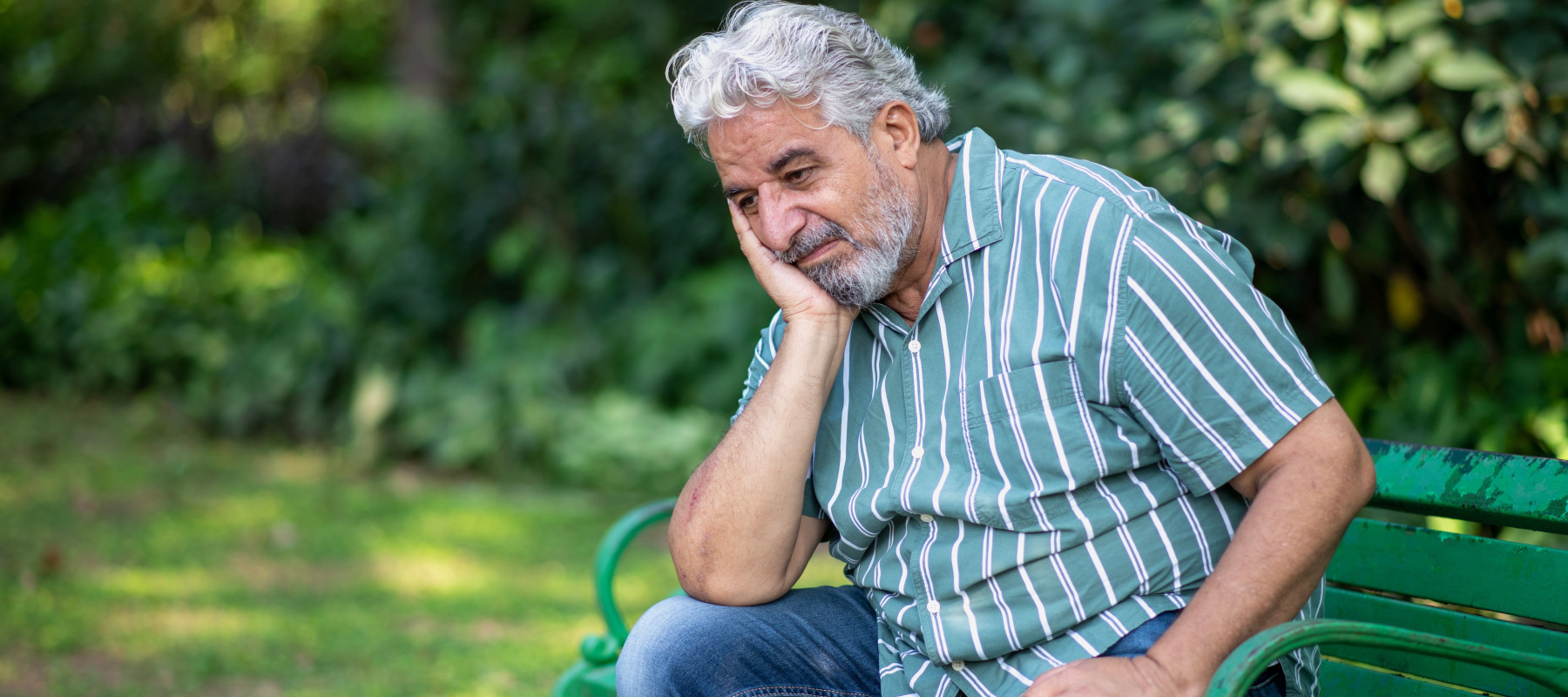 Old retired man sitting pensively on a park bench.
