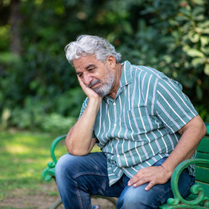 Old retired man sitting pensively on a park bench.