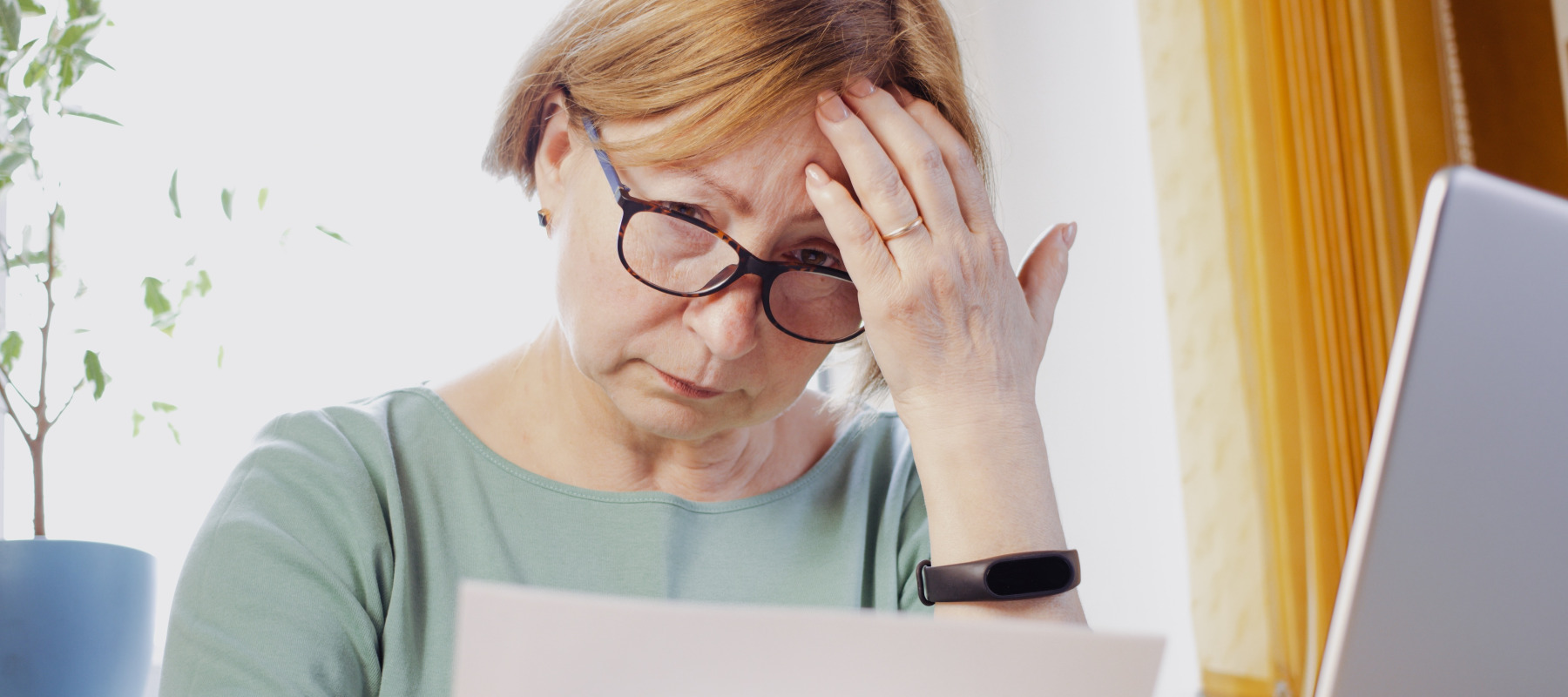 Worried mature woman reading paper document and feeling frustrated by unexpected bills.