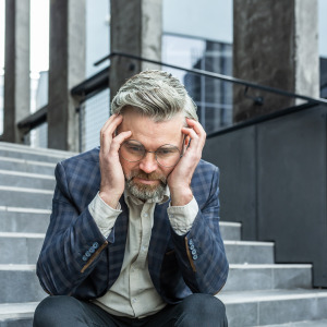 A man in a suit sits outside the courthouse on the steps and looks down, holding his head in his hands.