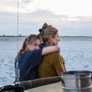 Mother and daughter seen from behind, daughter with her arms draped around the mother's neck lovingly.