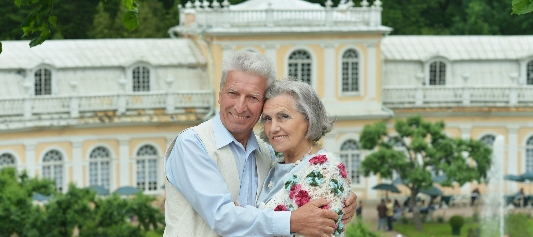 Portrait of a well-to-do older couple with a mansion in the background.