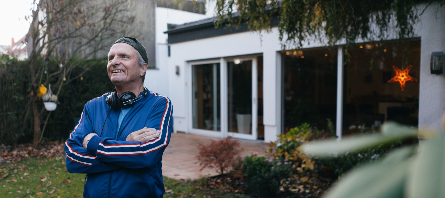 Man smiles, looking off camera with his arms crossed in the backyard of his home.