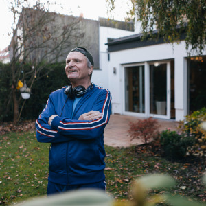 Man poses in his backyard, smiling with arms crossed, looking off to the side of the camera.