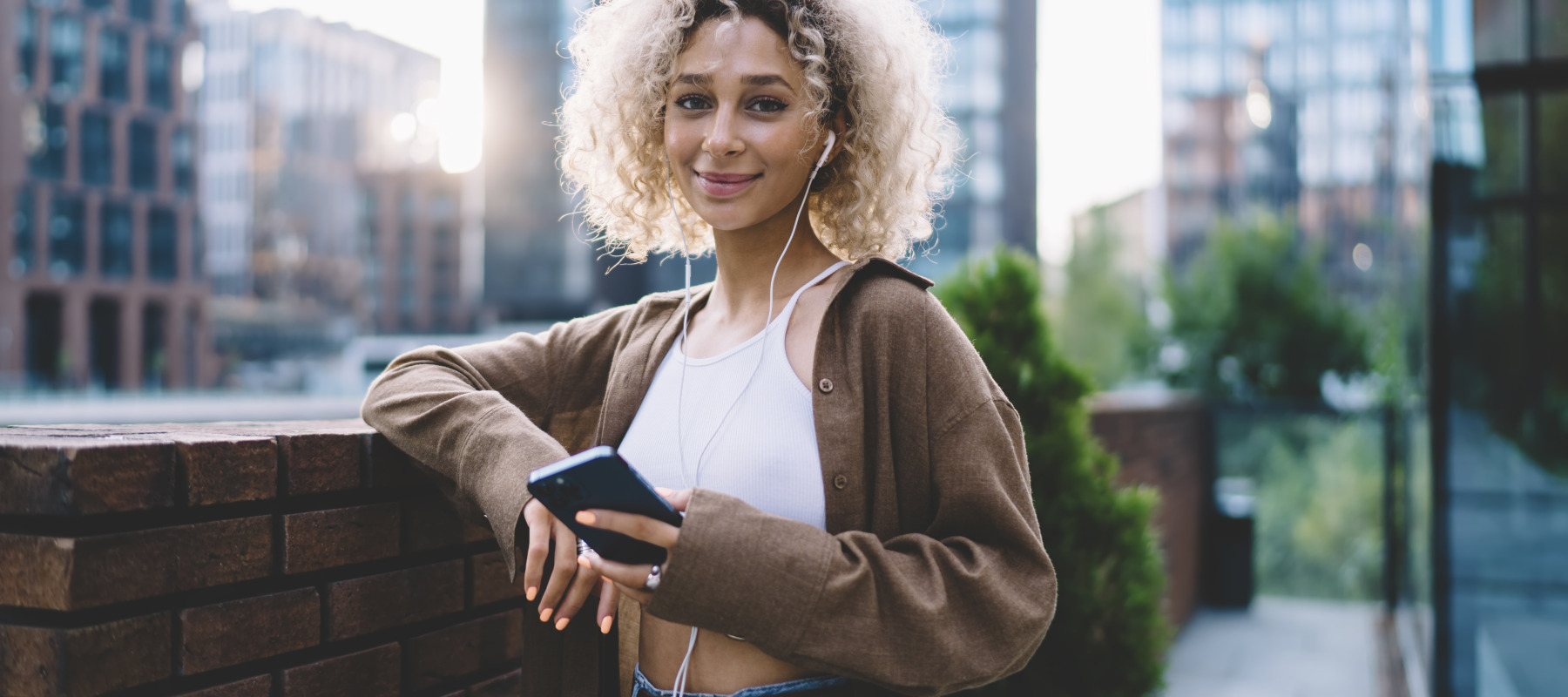 Young woman holding phone while smiling on the street