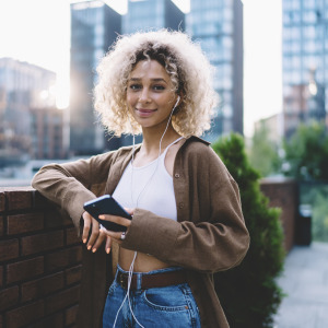 Young woman holding phone while smiling on the street