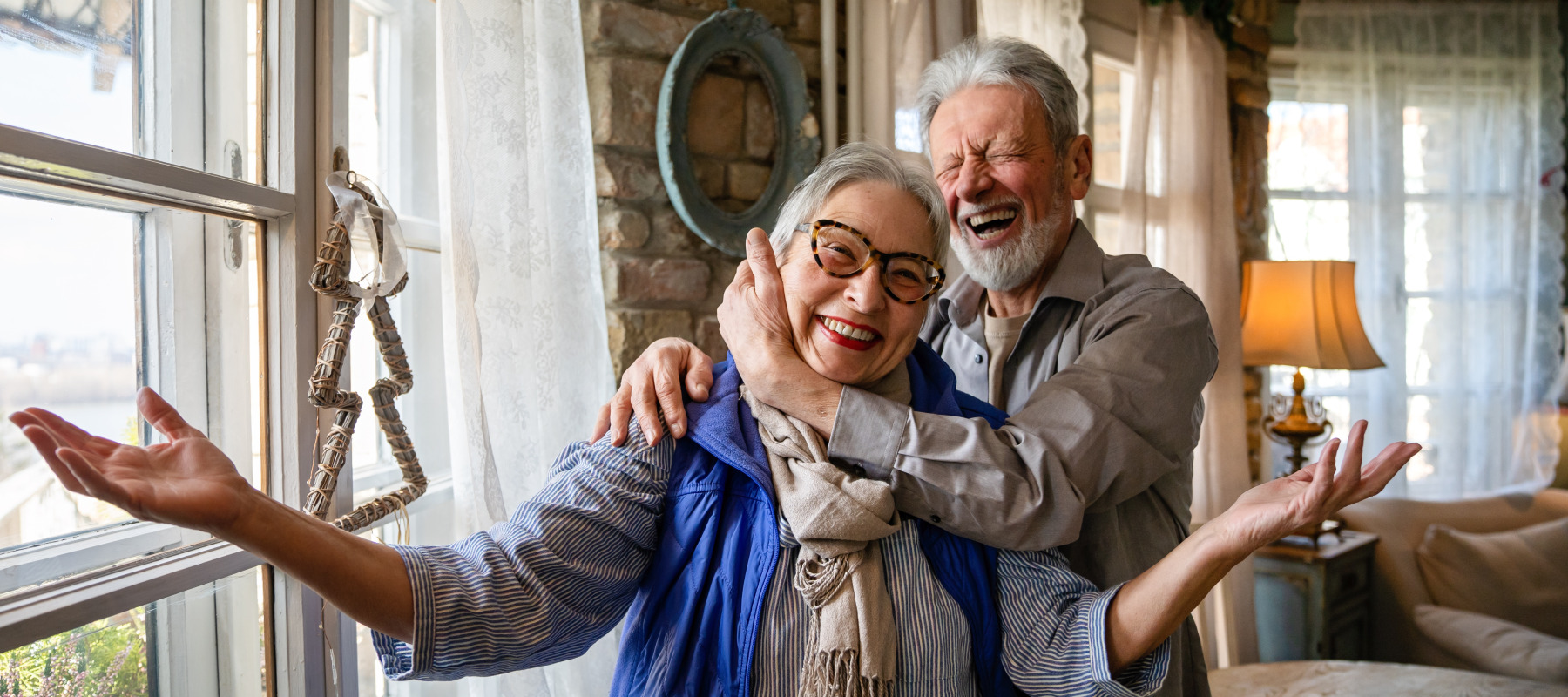 Happy senior couple embracing in their home. Laughing and smiling directly at the camera.
