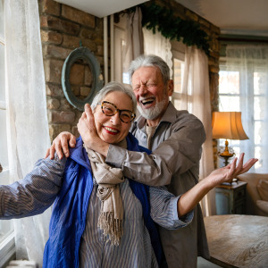 Happy senior couple embracing in their home. Laughing and smiling directly at the camera.