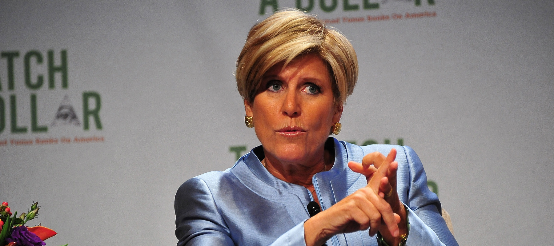 Suze Orman speaks on stage, looking serious and counting on her fingers.