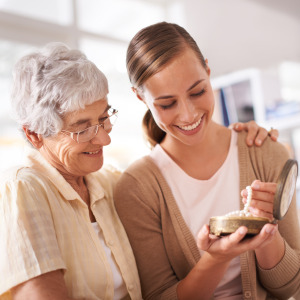 An elderly woman and a younger woman look happily at a piece of jewelry together.