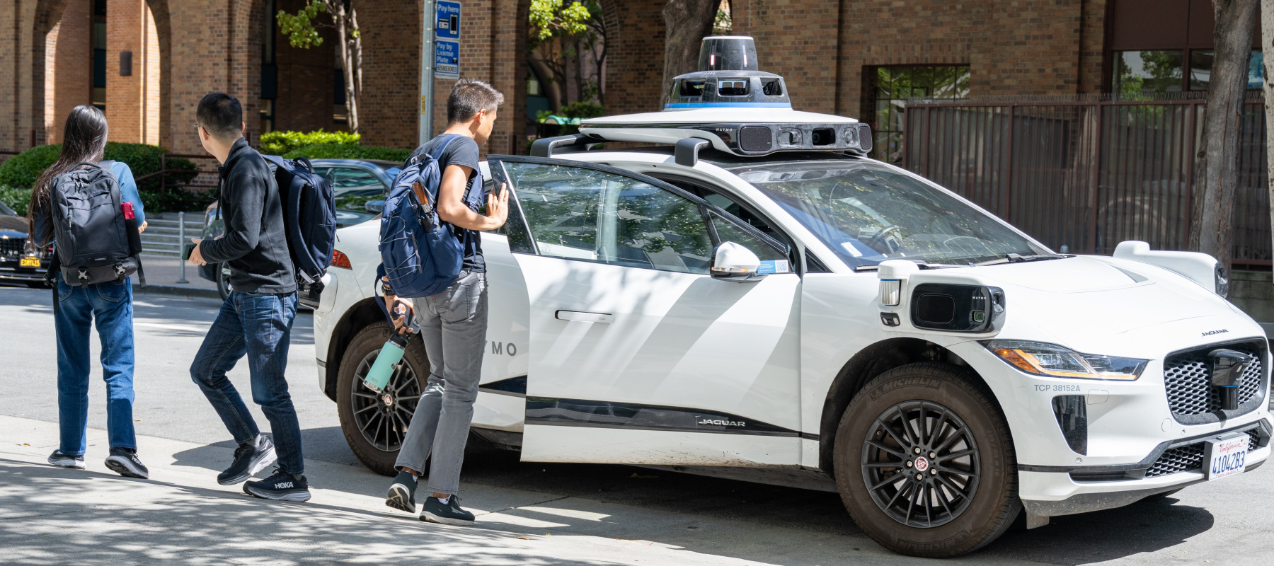 Pedestrians exit a parked Waymo self-driving car in front of Google's San Francisco headquarters.