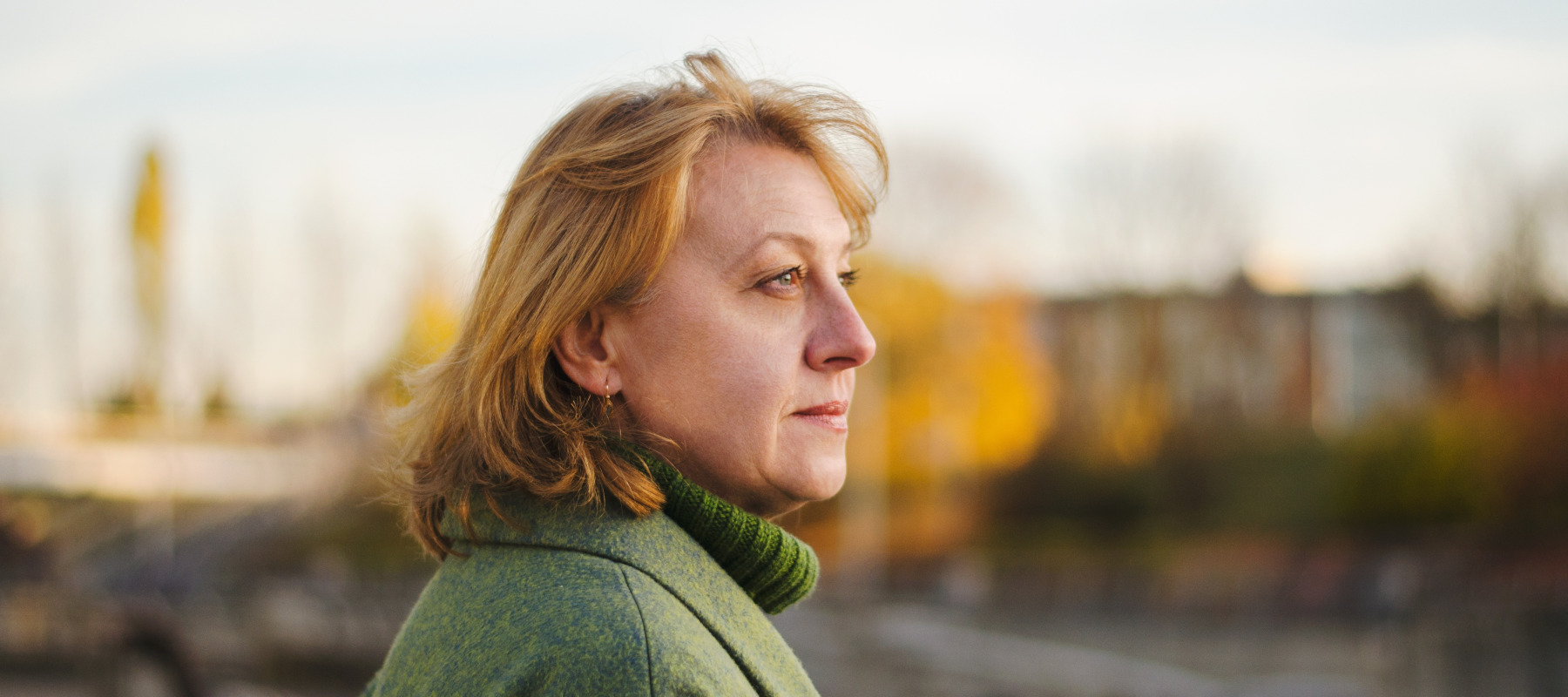 Woman in green coat looks off to the side of the camera, appears unhappy.