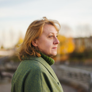 Woman in green coat looks off to the side of the camera, appears unhappy.