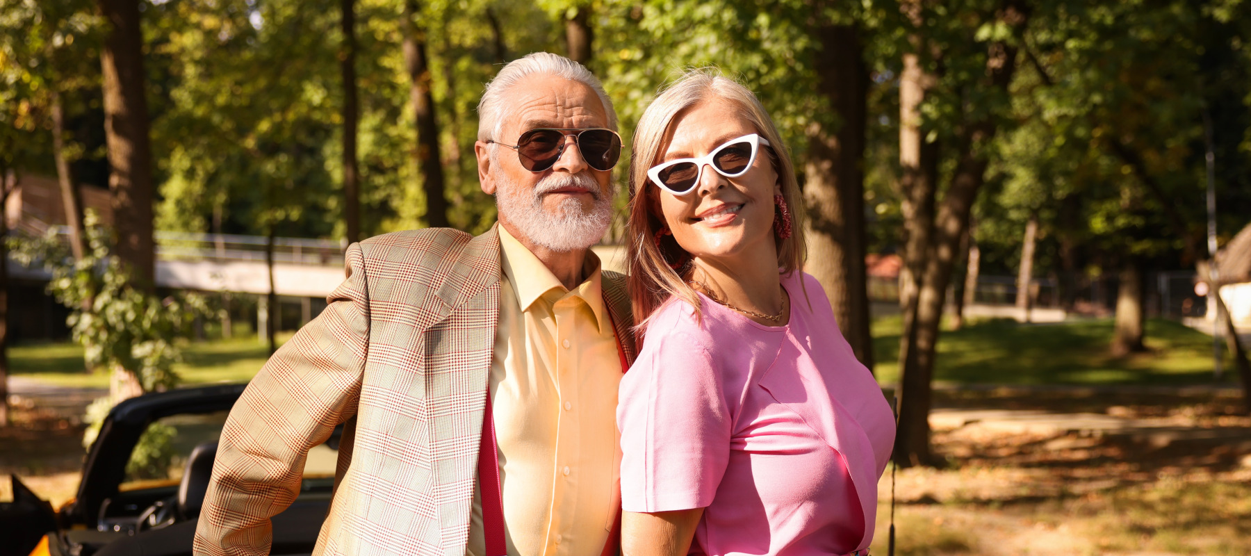 A stylish senior couple poses by a bright yellow convertible.