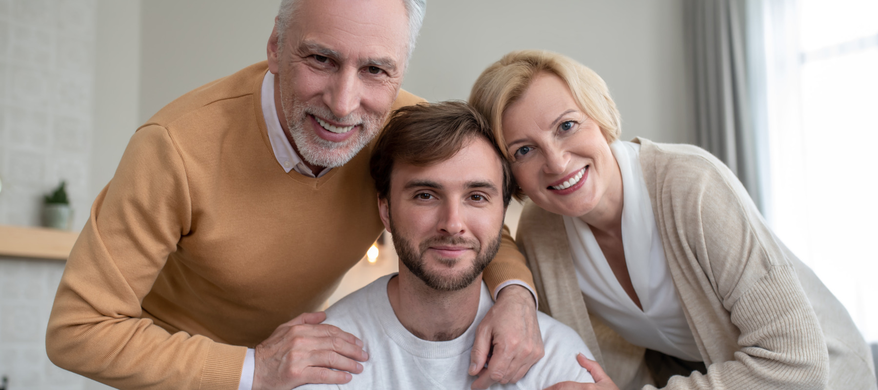 Two older parents embrace their adult child in a family home.