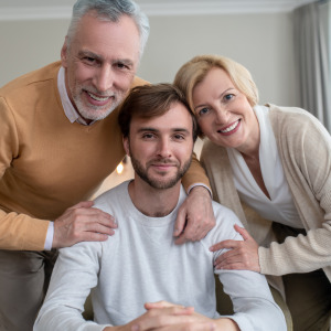 Two older parents embrace their adult child in a family home.