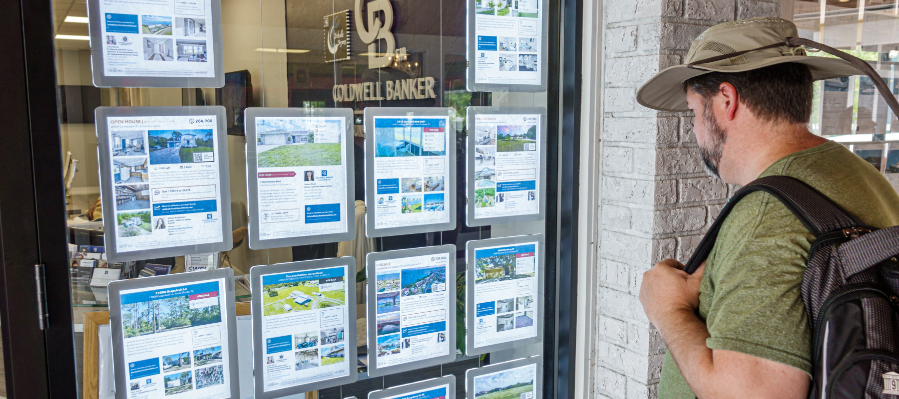 Man looks at real estate listings printed out and taped up in a real estate brokerage window.