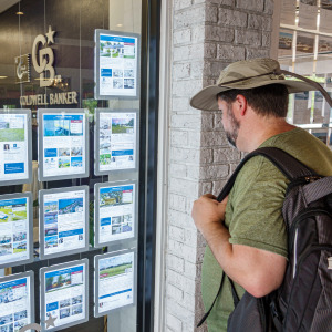 Man looks at real estate listings printed out and taped up in a real estate brokerage window.