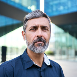 Man with salt-and-pepper hair looks directly at the camera, appears serious.