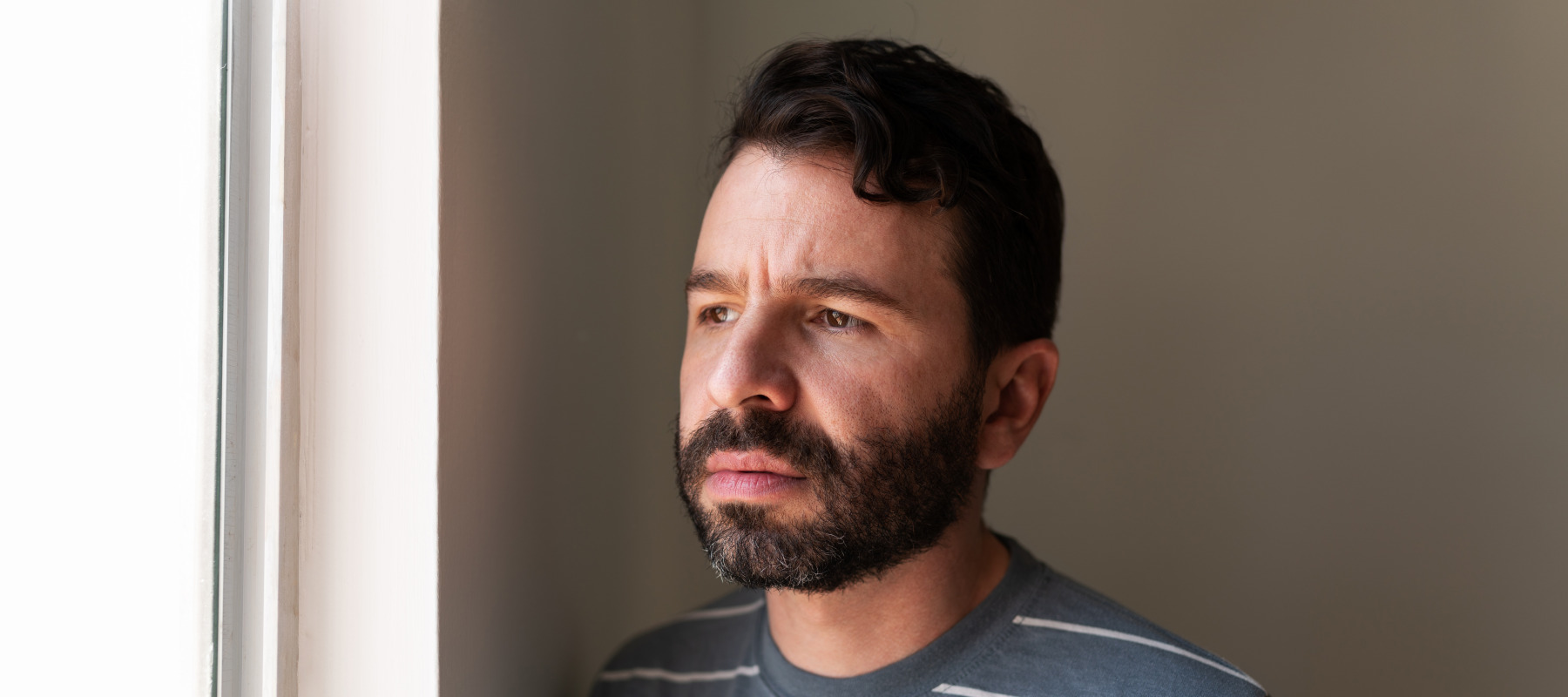 Man with a beard staring out the window contemplatively.
