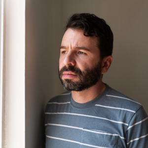 Man with a beard staring out the window contemplatively.