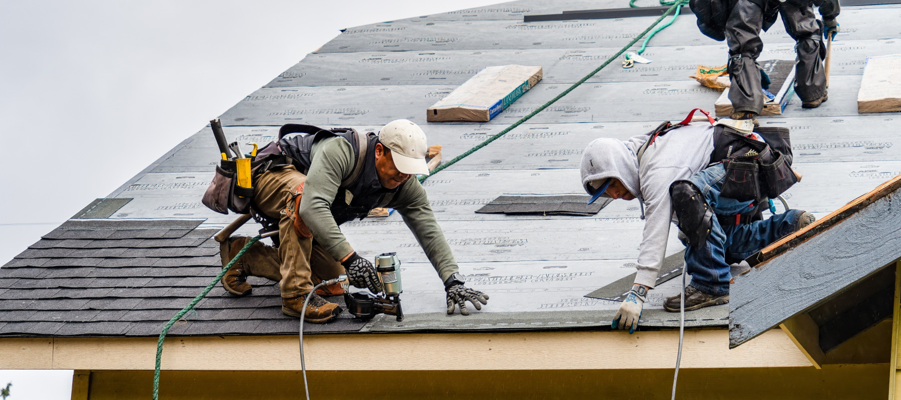 Contractor installs new shingles on roof on a rainy day.