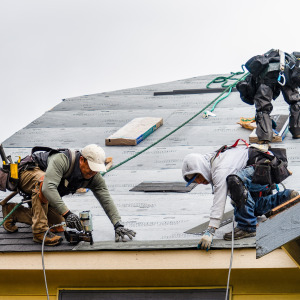 Contractor installs new shingles on roof on a rainy day.