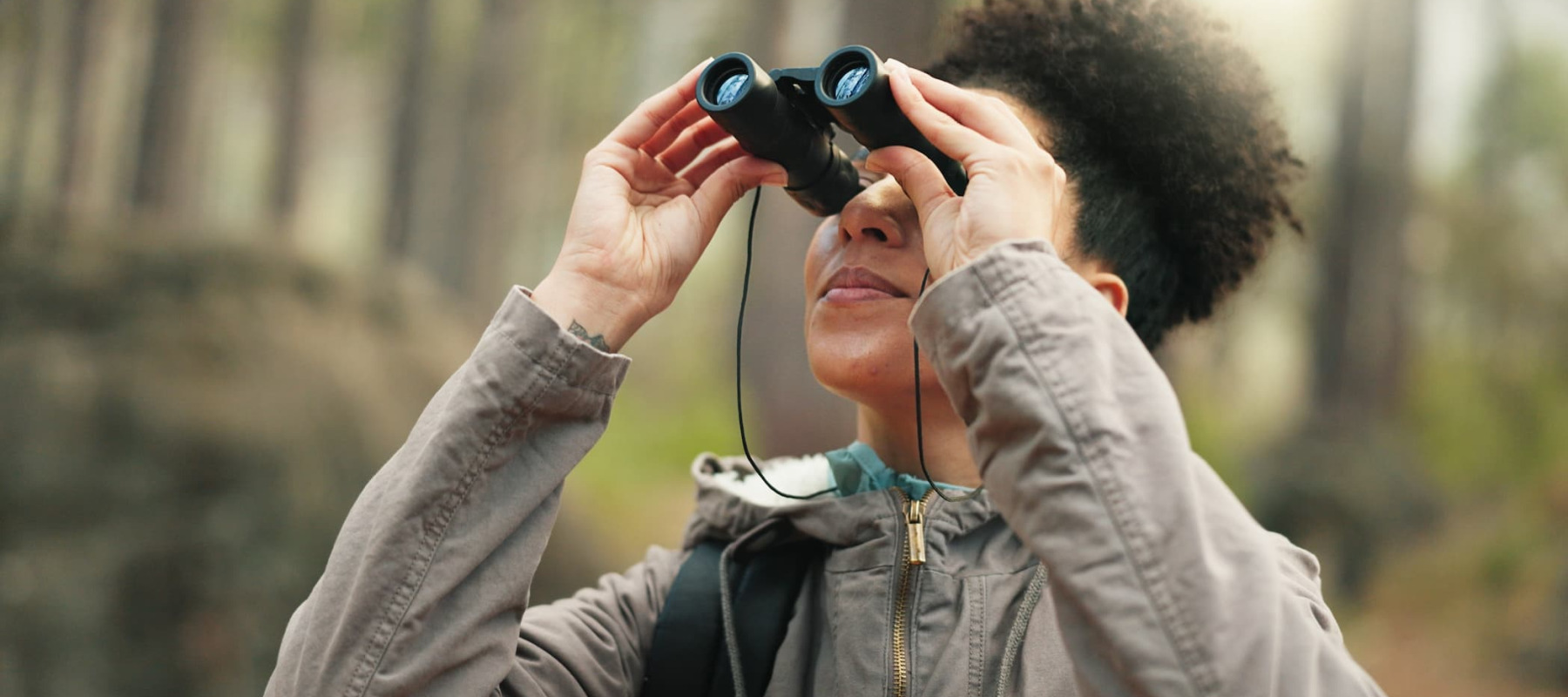 A photo of a woman looking into the forest through binoculars