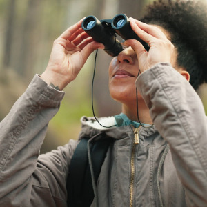 A photo of a woman looking into the forest through binoculars