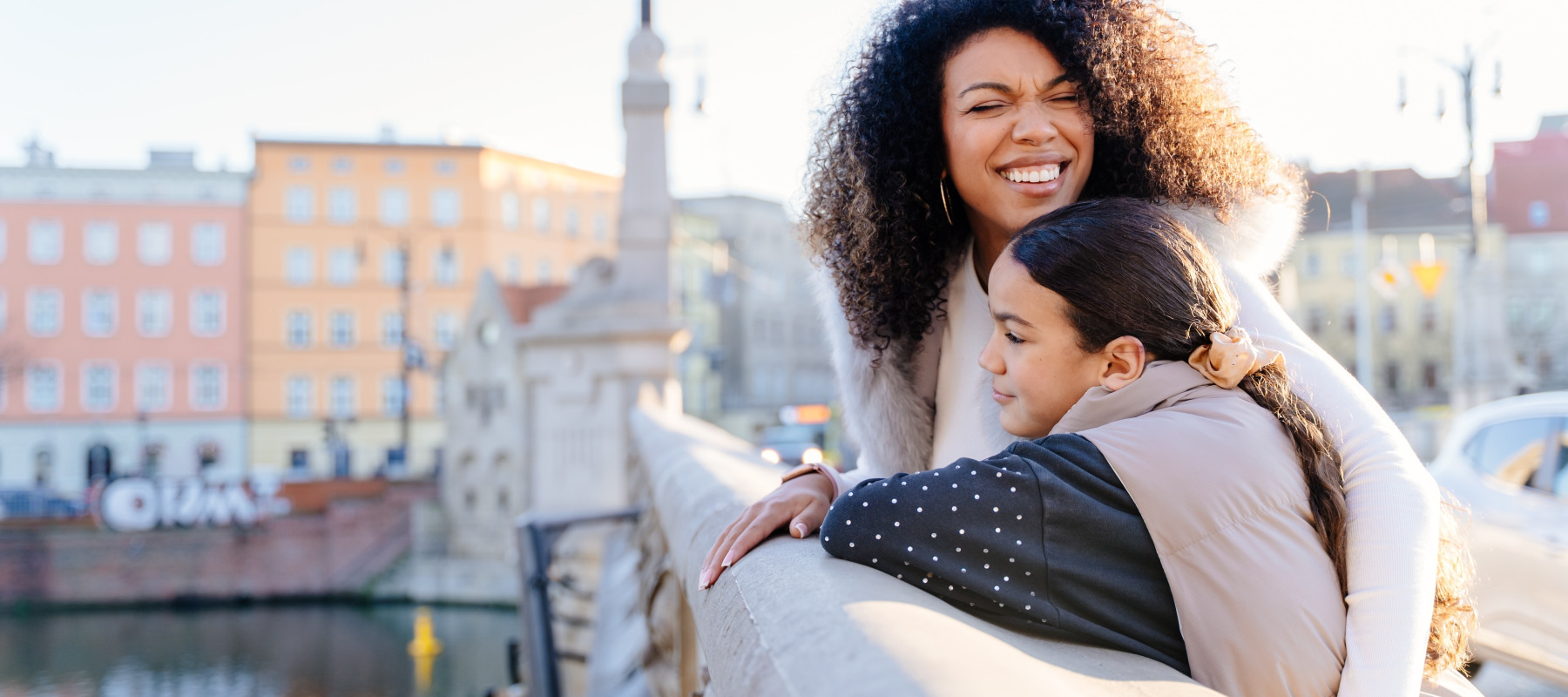 African-American mother hugs daughter on a bridge in Europe.