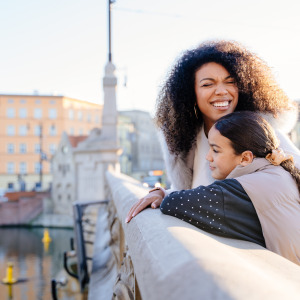 African-American mother hugs daughter on a bridge in Europe.