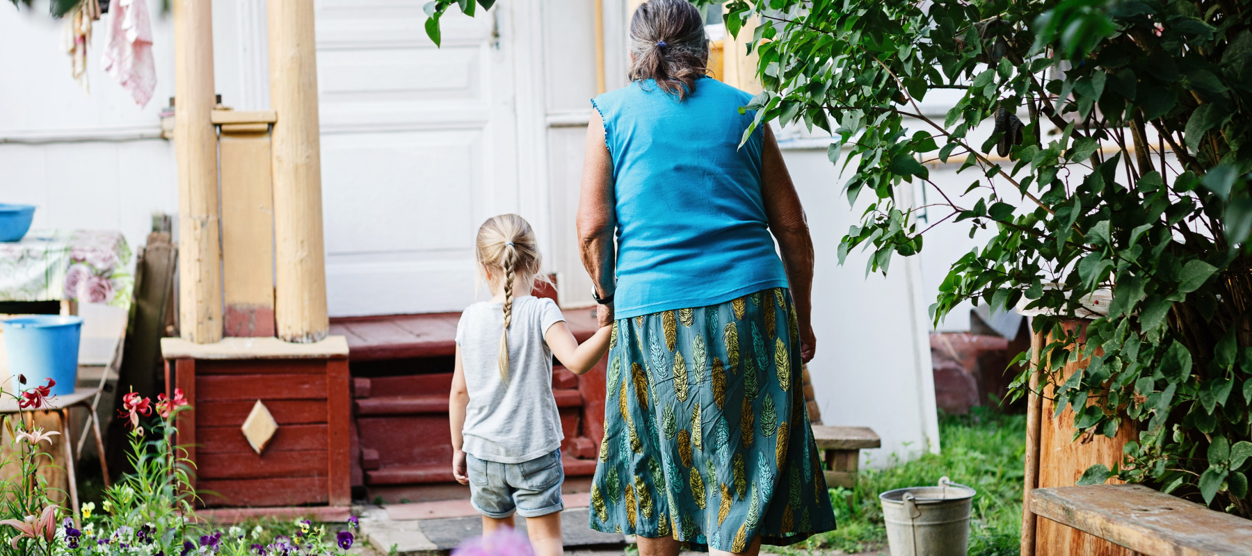 Grandmother holding her granddaughter's hand and walking towards her house