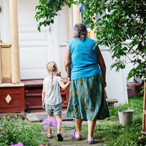 Grandmother holding her granddaughter's hand and walking towards her house