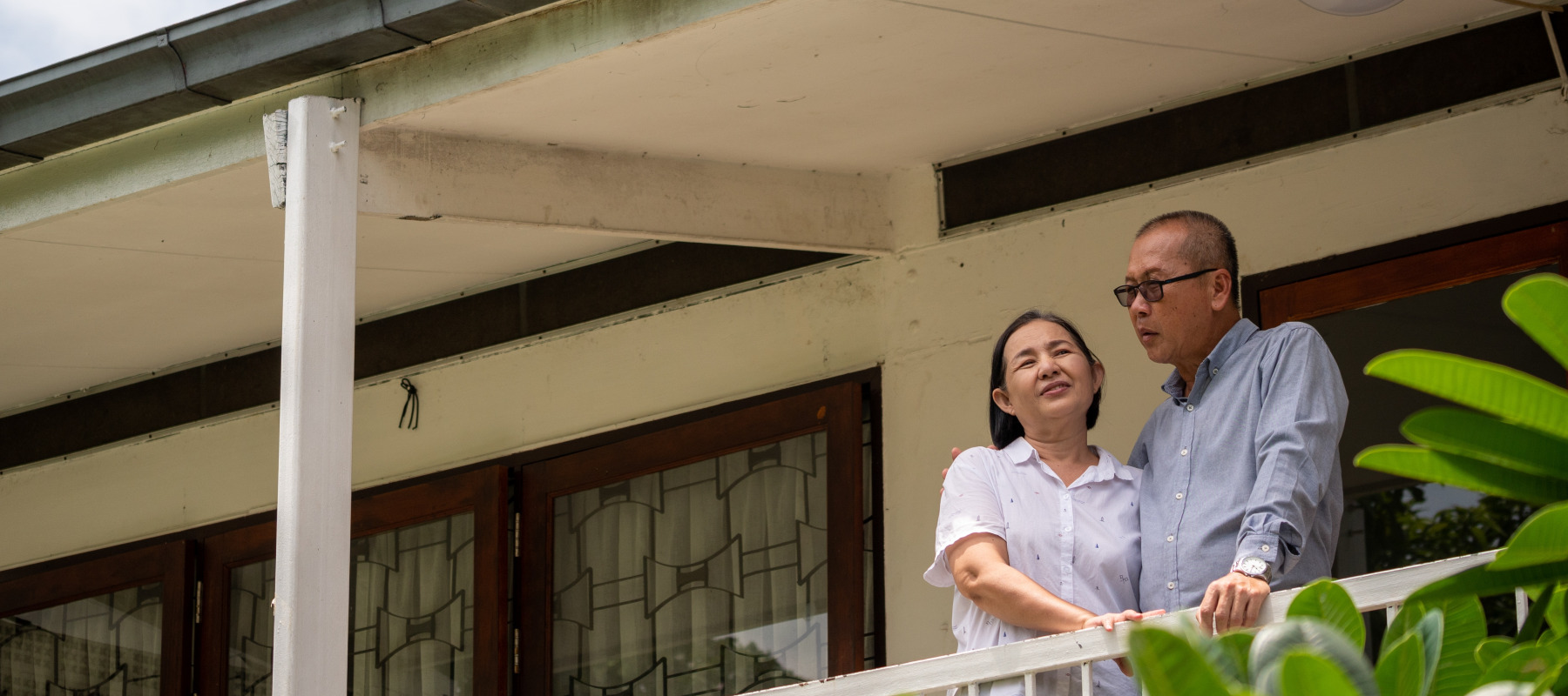 Older couple seen on a balcony outside their home, talking to each other and not looking at the camera directly.