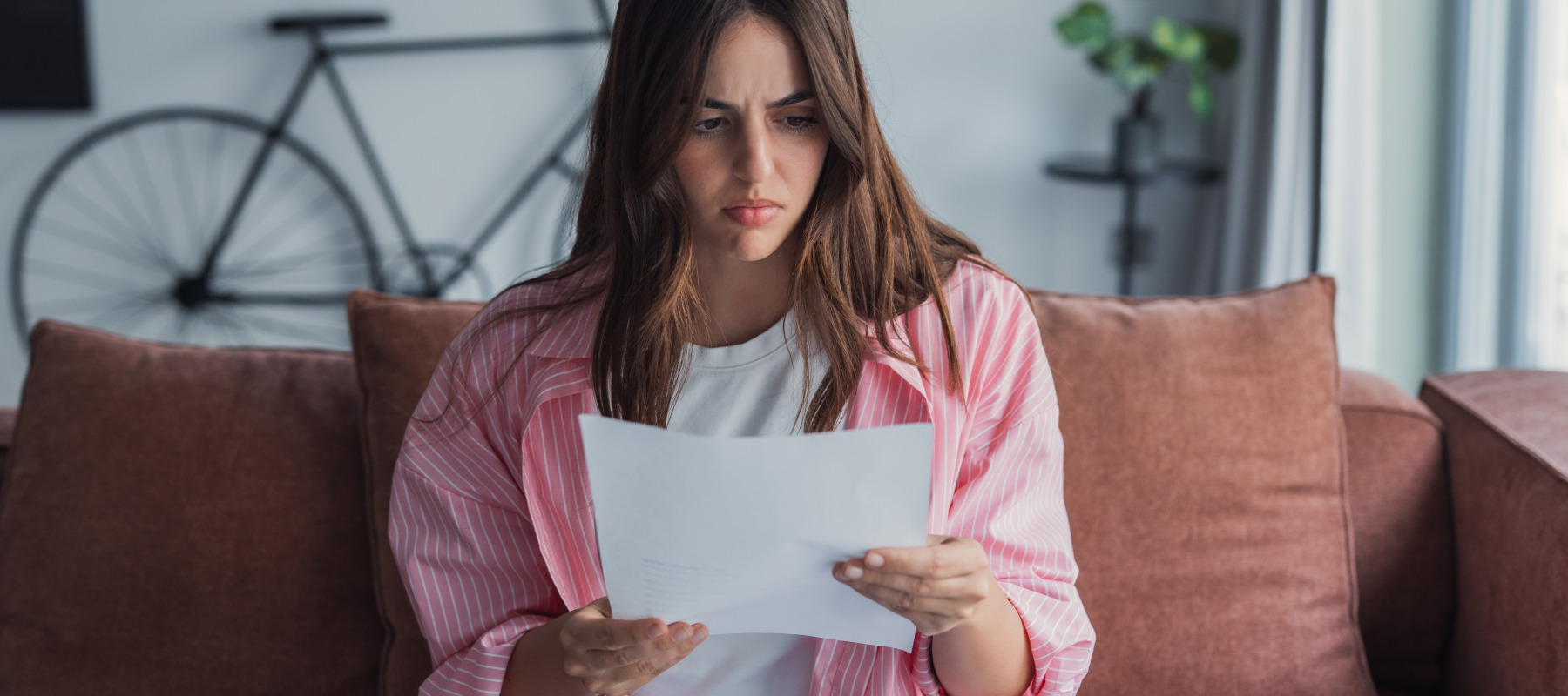 Worried young Caucasian woman reads over a letter with bad news.