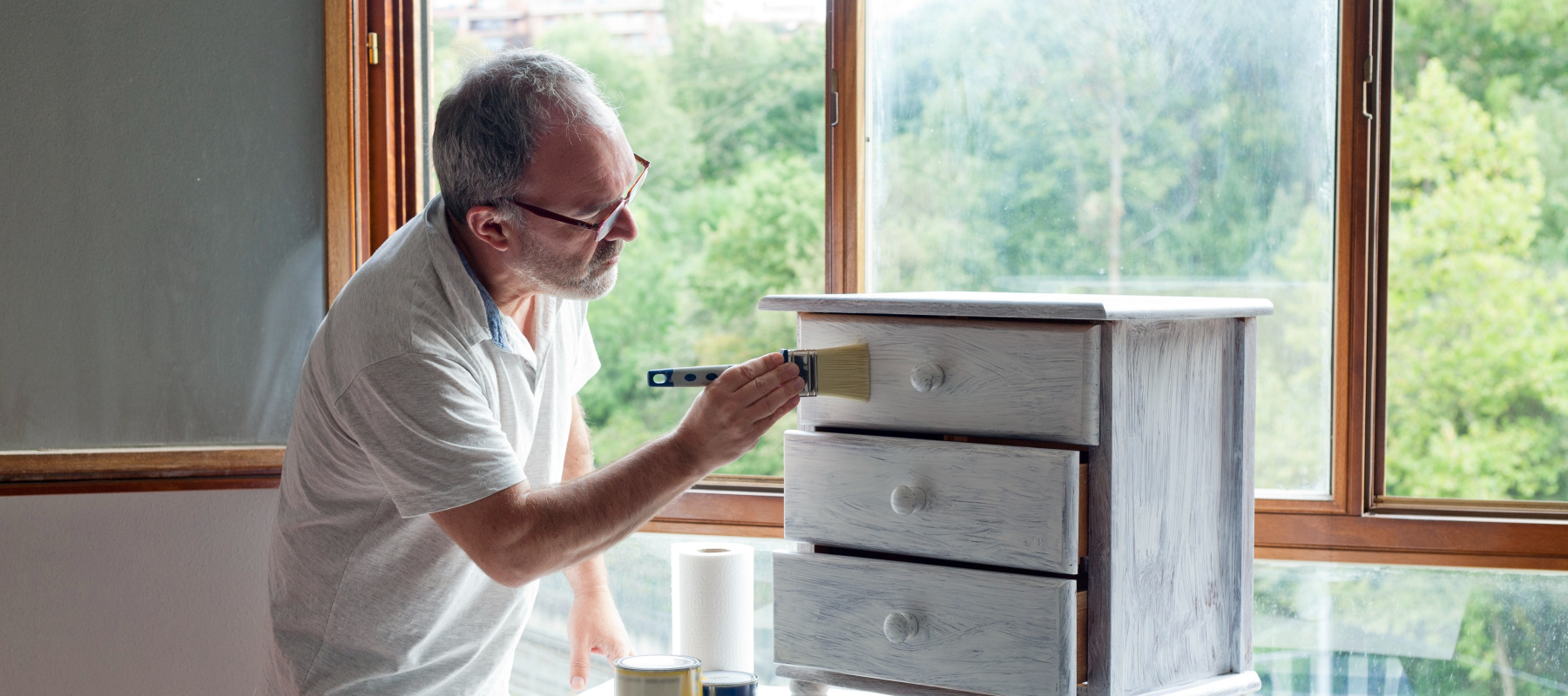 Older man seen painting a dresser white.