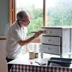 Older man seen painting a dresser white.