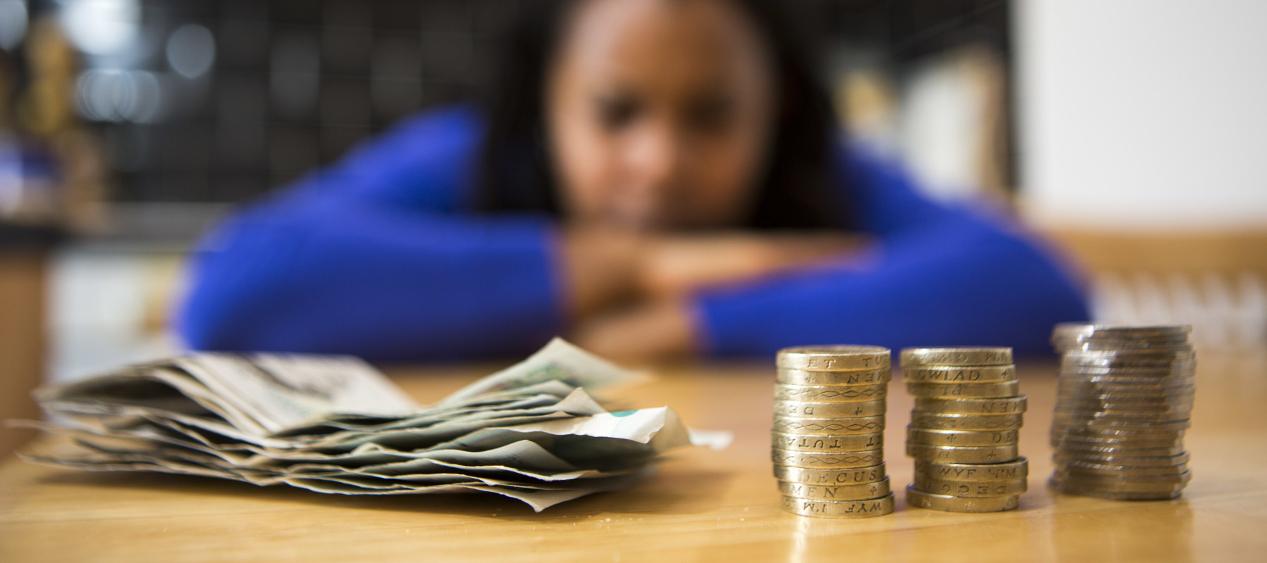 Woman sits at her kitchen table with bank notes and coins in front of her.