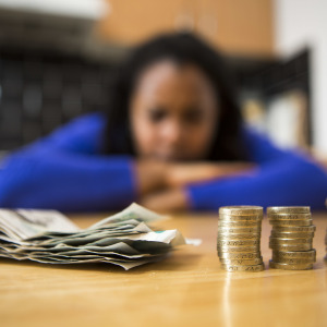 Woman sits at her kitchen table with bank notes and coins in front of her.