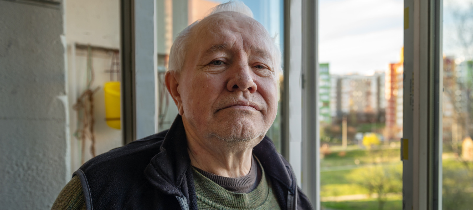Portrait of a sad elderly man looking out the window at home. Lonely elderly man looking out the window.