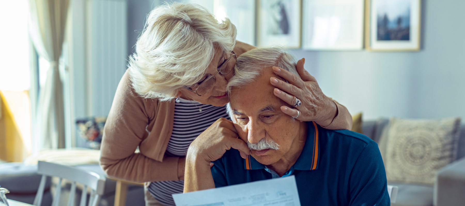 An older couple sit at their kitchen table, sorting through bills.