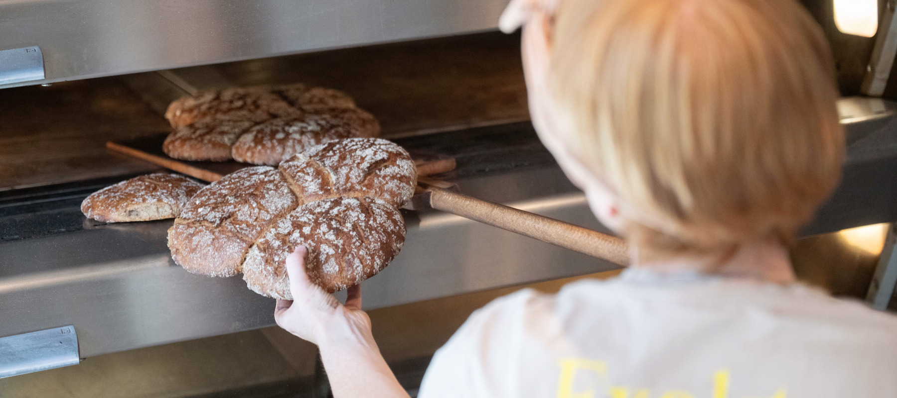 A baker takes sourdough bread out of an oven.