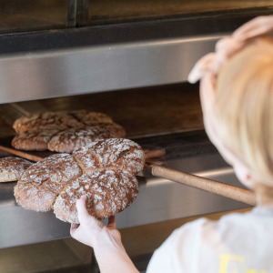 A baker takes sourdough bread out of an oven.
