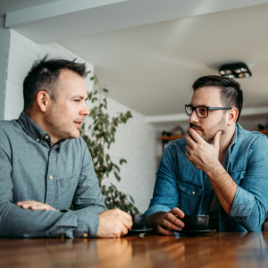 Two adult brothers have serious discussion at kitchen table