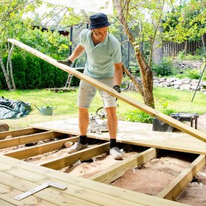 A man building a wooden deck in his backyard.