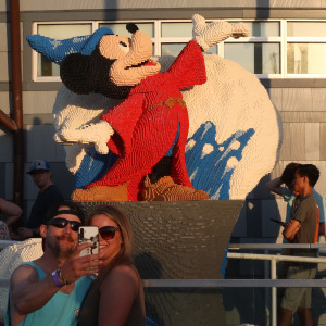 Visitors to Disney Springs take a selfie in front of a Fantasia Mickey statue made of Lego.