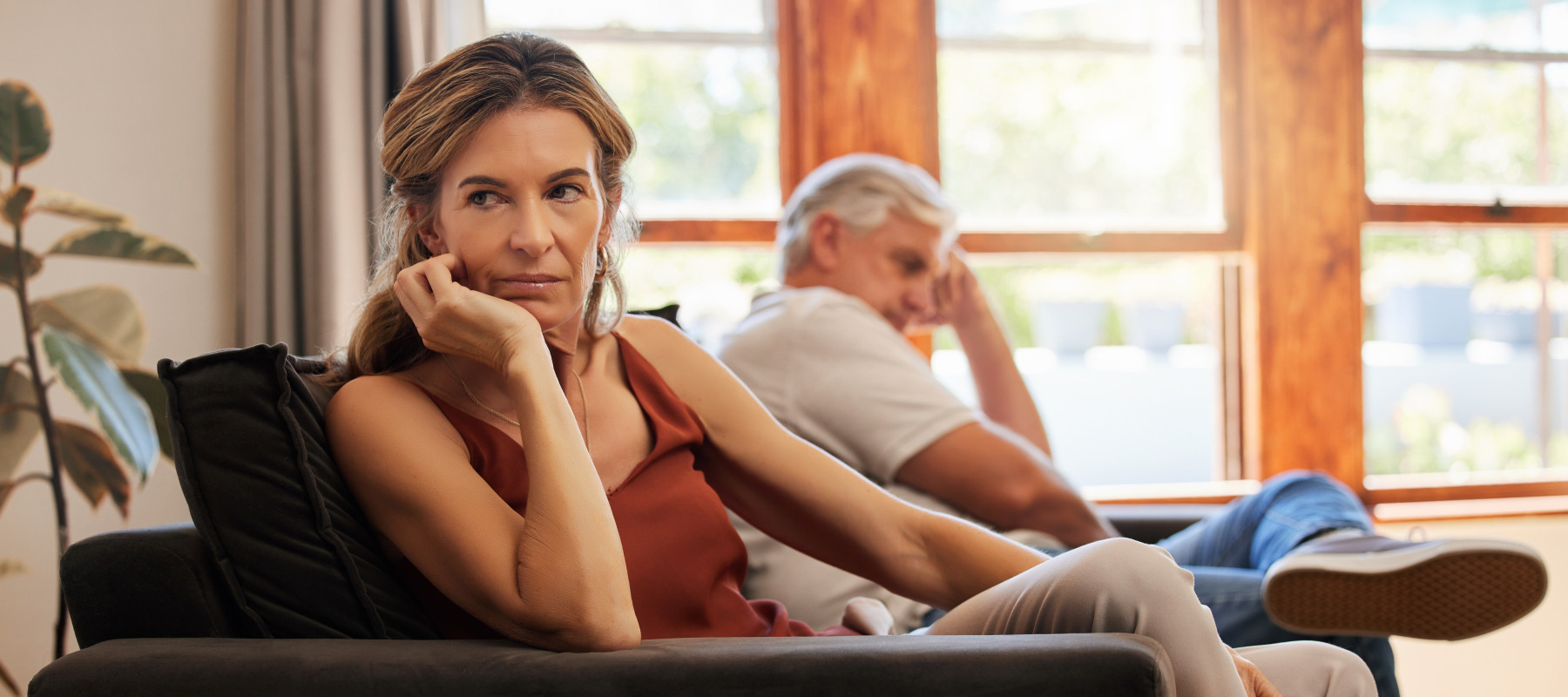 Older couple sit on the couch, looking upset and away from each other.