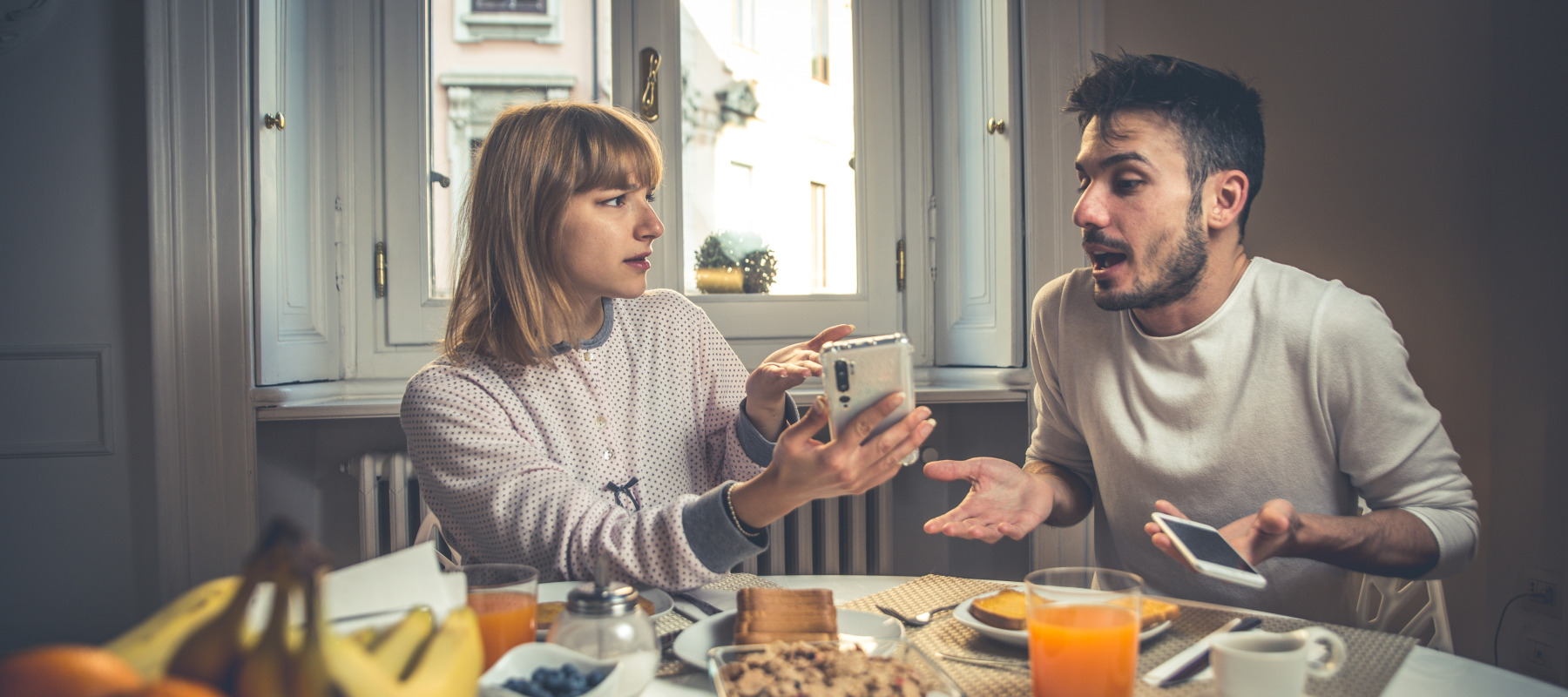 Upset couple argue over a phone at the breakfast table.