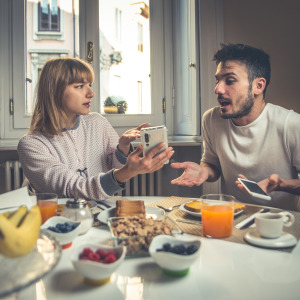 Upset couple argue over a phone at the breakfast table.